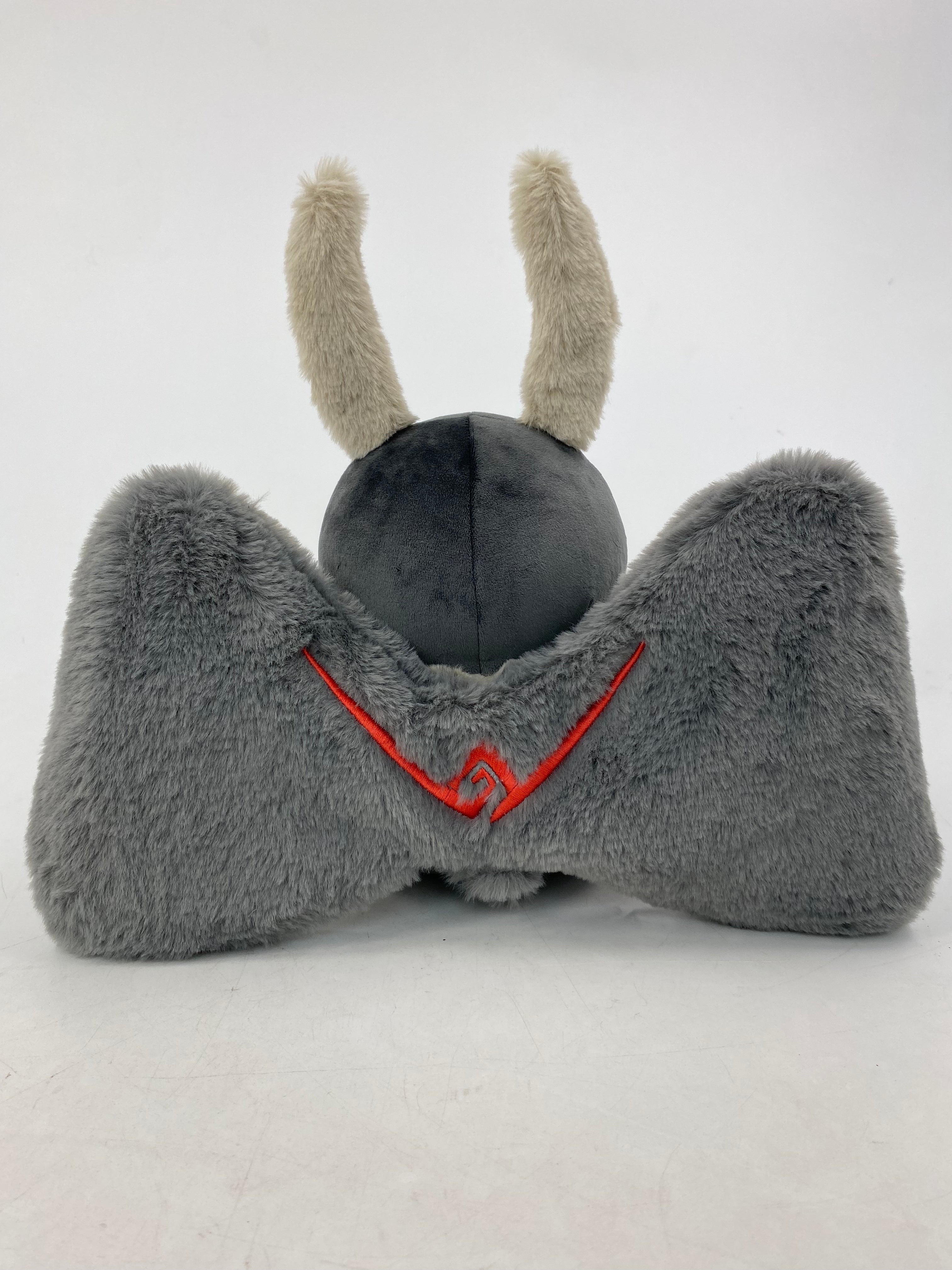Motthew the Mothman plush by TOTYM, inspired by West Virginia folklore, with fluffy antennae, wings, and glowing red eyes, shown from the back on a white background.