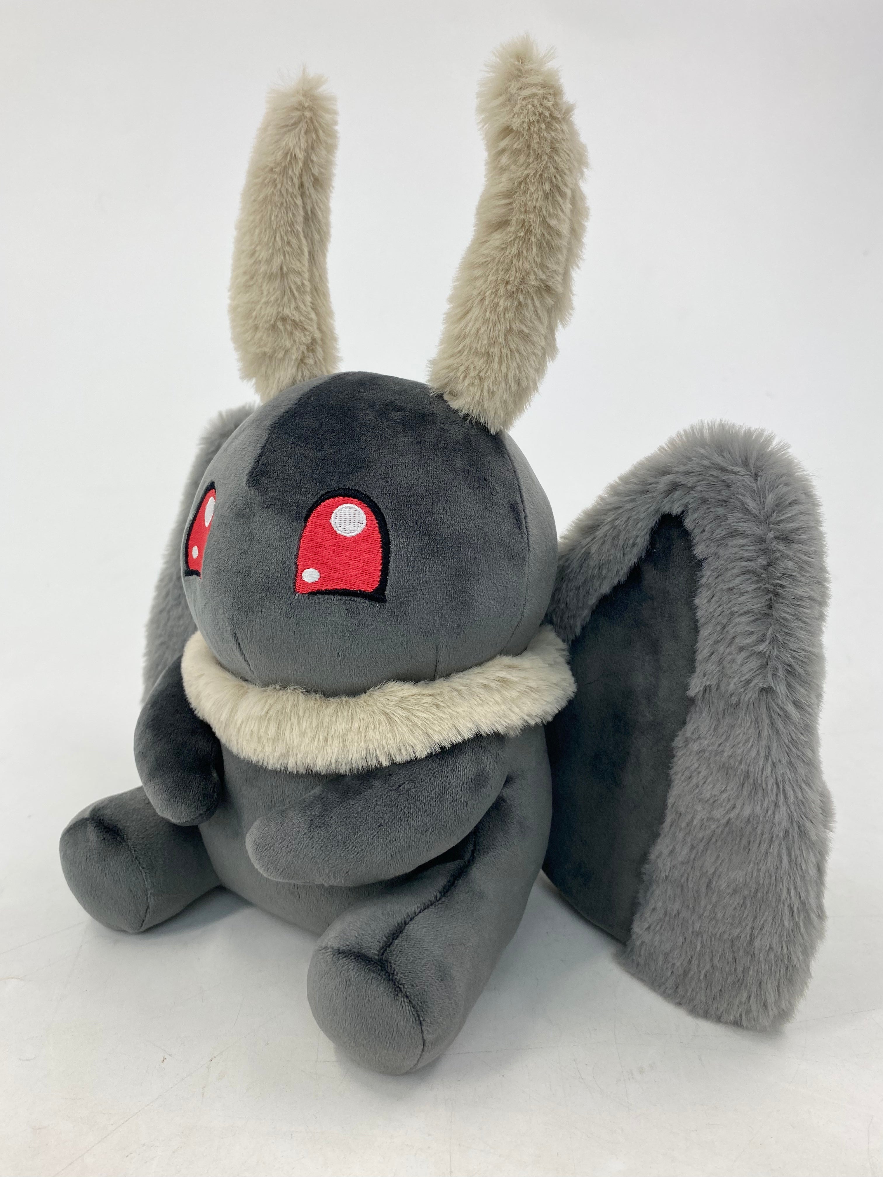 Motthew the Mothman plush by TOTYM, inspired by West Virginia folklore, with fluffy antennae, wings, and glowing red eyes, facing a left angle on a clean white background.