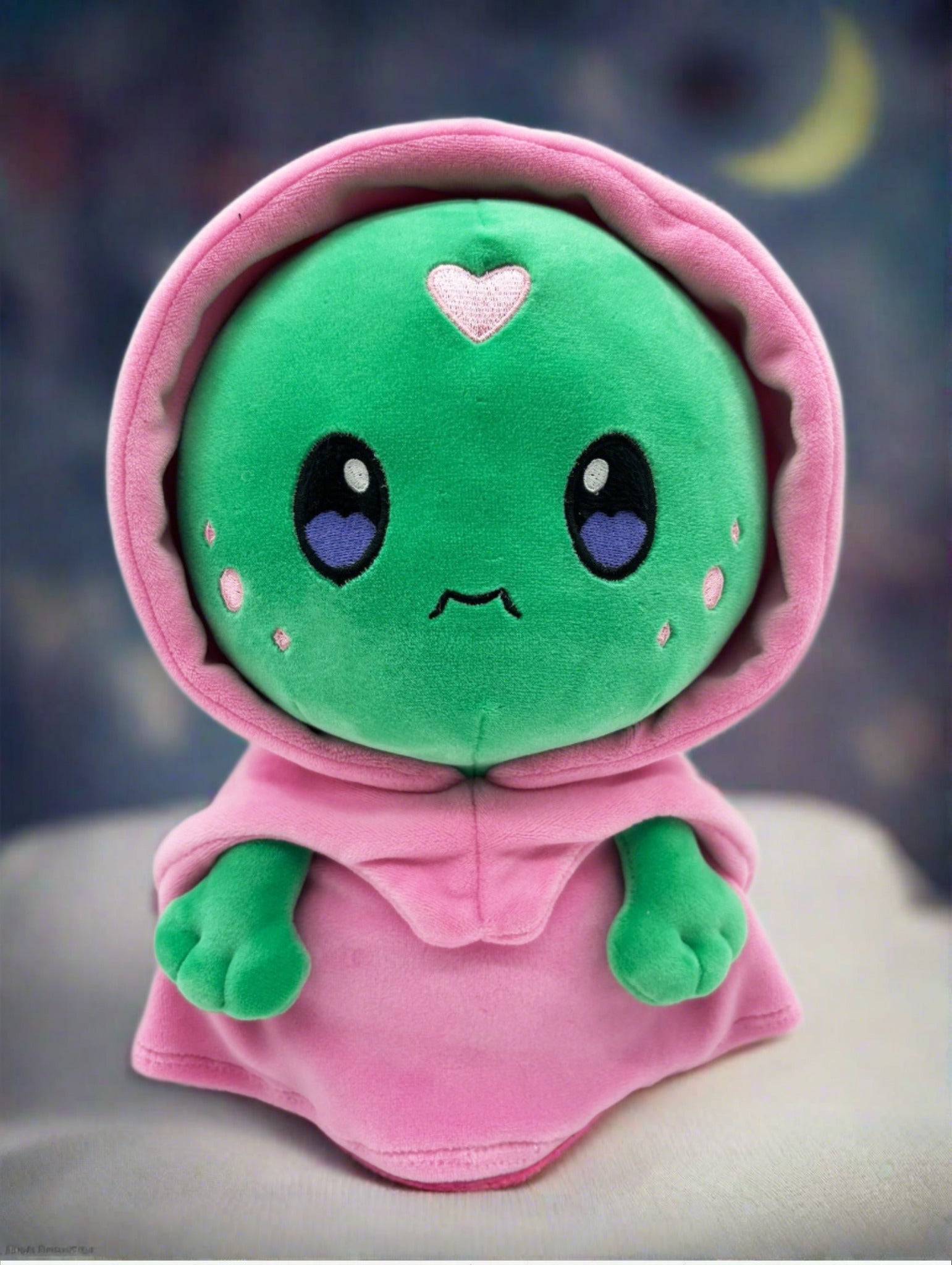 TOTYM's Dreamwalker plush featuring a cute green face, purple heart eyes, and wearing a pink hooded cloak. Designed in a kawaii style for collectors of mythical creature plush toys.